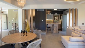 Uma sala de estar moderna com uma mesa de madeira redonda, um sofá e uma área de cozinha ao fundo.