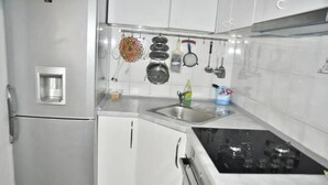 A compact kitchen with white cabinets, a built-in refrigerator, a stove, and various utensils hanging on the wall. - Park Apartment (Split)