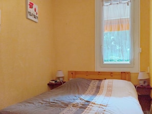Una camera da letto con un letto, una finestra con tende, un comodino con una lampada e un quadro appeso al muro.