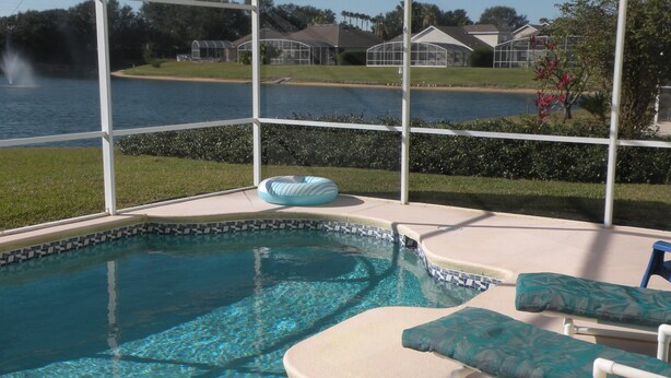 Un área de piscina con vista despejada a un lago, una sección cubierta y sillones de descanso.