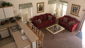 Una sala de estar con un sofá rojo, una mesa de centro de vidrio y una zona de cocina con un fregadero y una mesa de comedor.