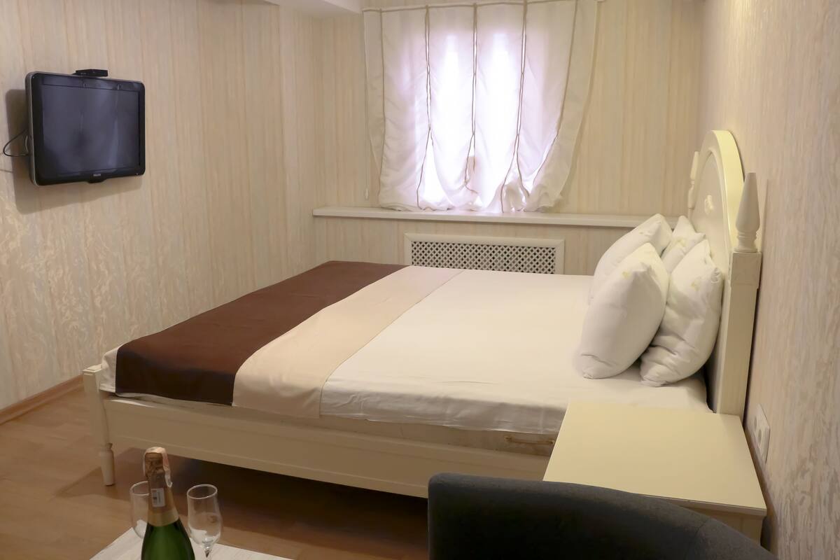 A hotel room with a bed, a bedside table, a chair, a TV, and a window with curtains.