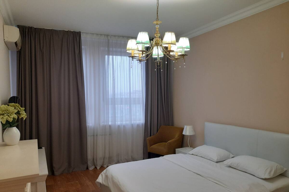 A hotel room with a bed, a chair, a desk, a lamp, and a chandelier.