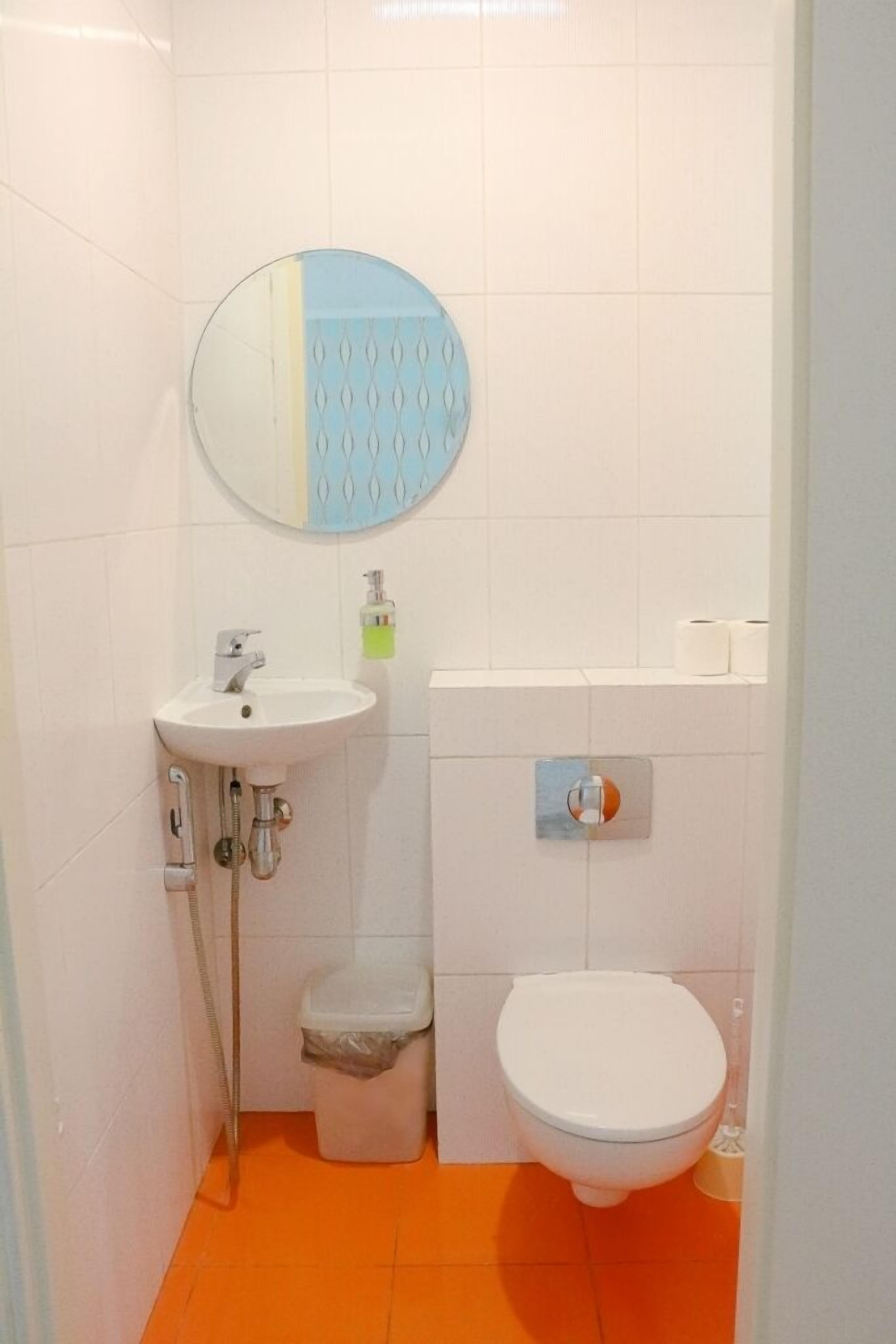 Een badkamer met een witte wastafel, een ronde spiegel, een toilet en een oranje vloer.