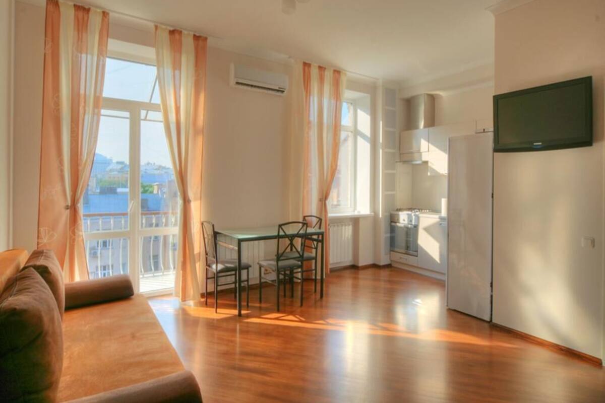 A spacious living area with a wooden floor, a sofa, a dining table with chairs, and a kitchen area with a stove and cabinets.