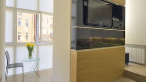 Una cuina moderna amb televisió integrada, taula de vidre petita amb una cadira i vista a la ciutat a través de grans finestres.