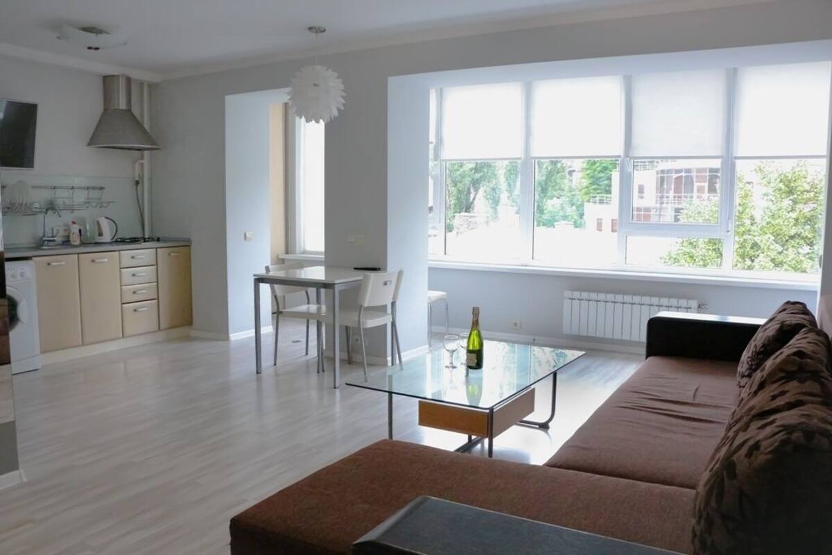 A modern living room with a glass coffee table, a sofa, and a dining area with a table and chairs.