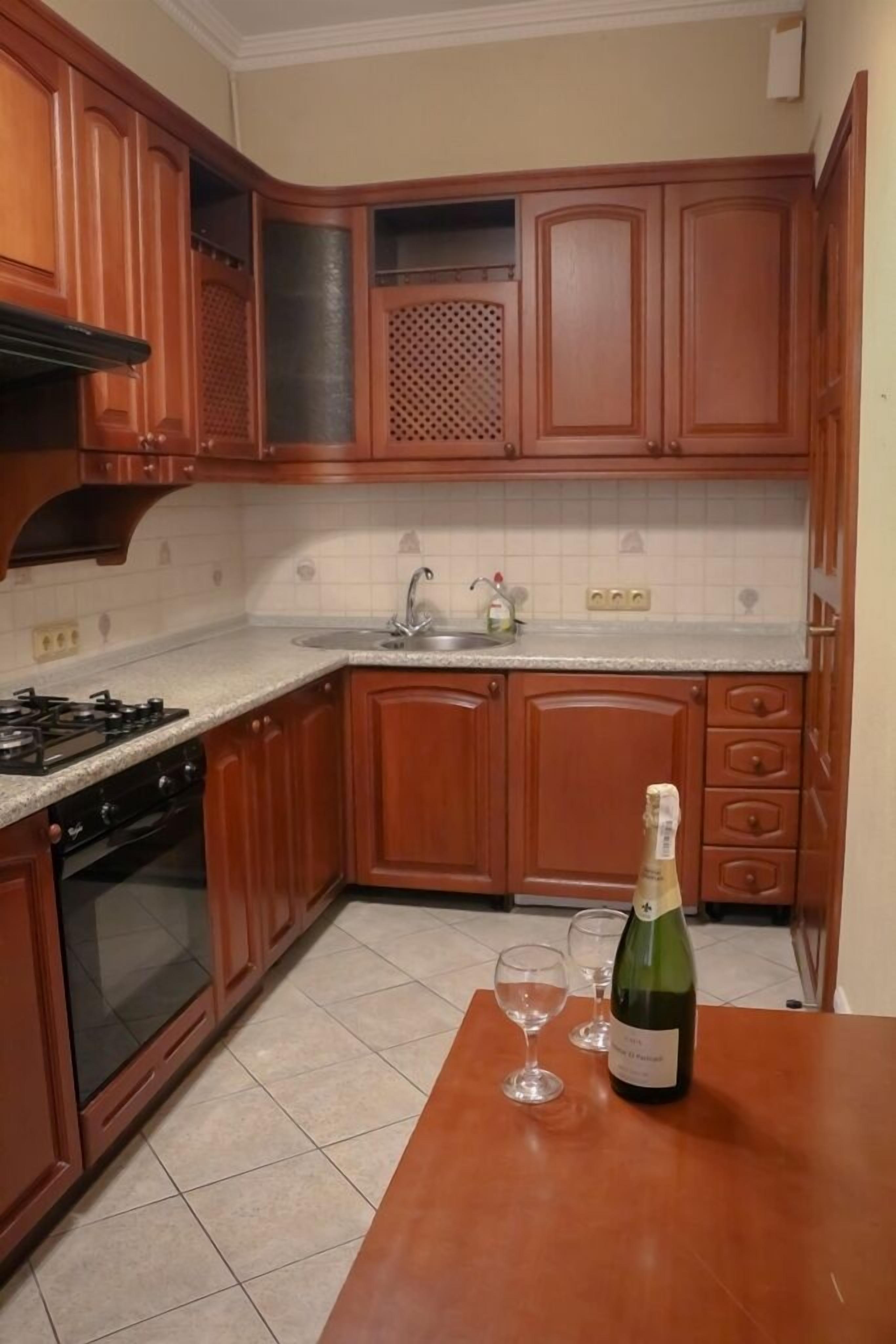 A kitchen with wooden cabinets, a gas stove, a sink, and a table with a bottle and glasses.