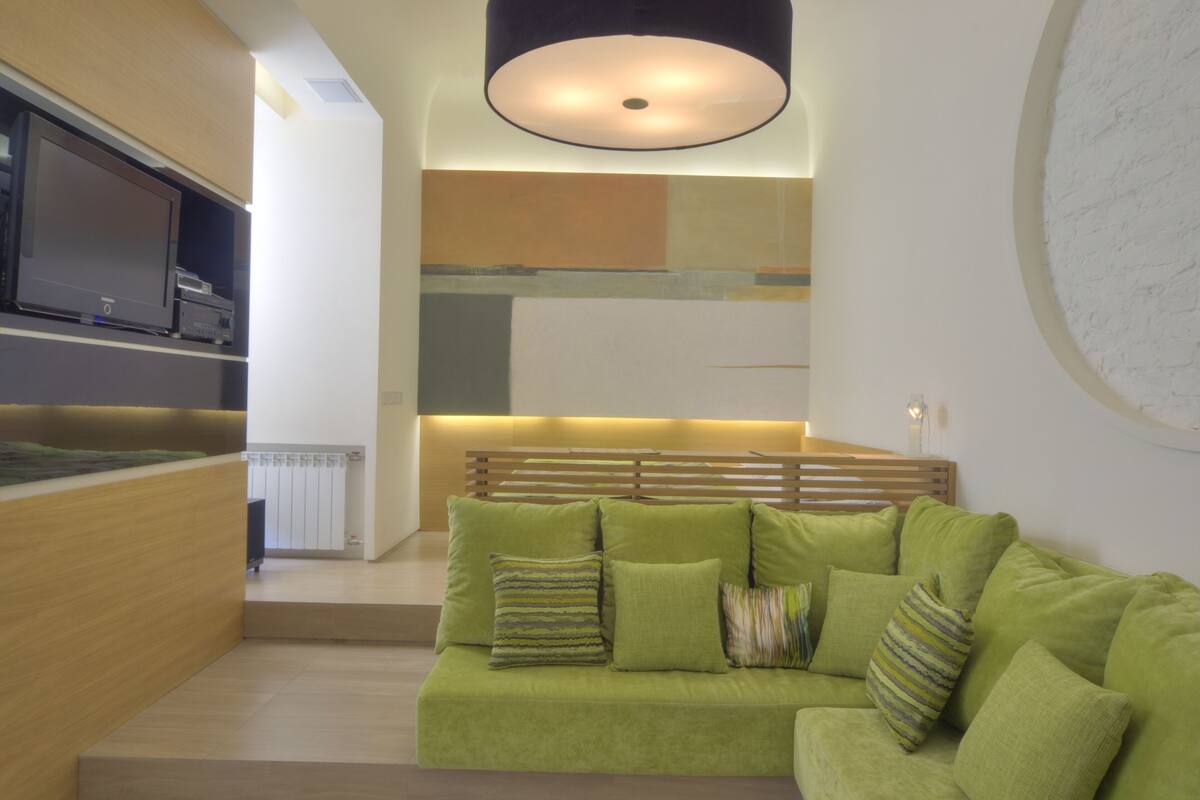 A modern living room with a green sofa, wooden headboard, and a large circular wall decoration.