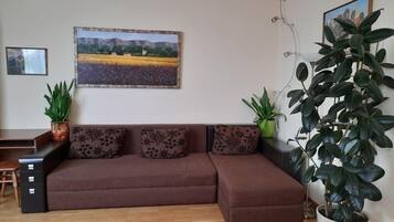 Ein Wohnzimmer mit einem braunen Sofa, zwei Blumentöpfen und einem Bild an der Wand.
