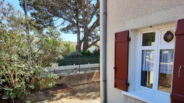 A building with a window and a door, a concrete pathway, and a green fence in the background. - Cozy Apartment with Private Courtyard, Near Shops and Beaches in Capbreton (Capbreton)