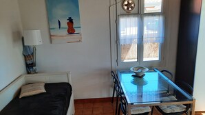 A room with a bed, a dining table with chairs, a window with curtains, a painting on the wall, and a lamp. - Cozy Apartment with Private Courtyard, Near Shops and Beaches in Capbreton (Capbreton)