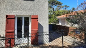 A building with a red door and shutter, a metal fence, and a clear blue sky. - Cozy Apartment with Private Courtyard, Near Shops and Beaches in Capbreton (Capbreton)