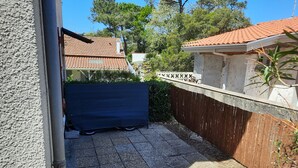 A covered outdoor area with a tiled floor, a wooden fence, and a building with a tiled roof. - Cozy Apartment with Private Courtyard, Near Shops and Beaches in Capbreton (Capbreton)