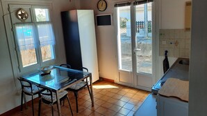 A kitchen with a dining table, chairs, a refrigerator, a clock, and a view through the door. - Cozy Apartment with Private Courtyard, Near Shops and Beaches in Capbreton (Capbreton)
