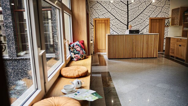 Un moderno vestíbulo de hotel con mostrador de recepción, zona de estar con cojines y un muro con diseño.