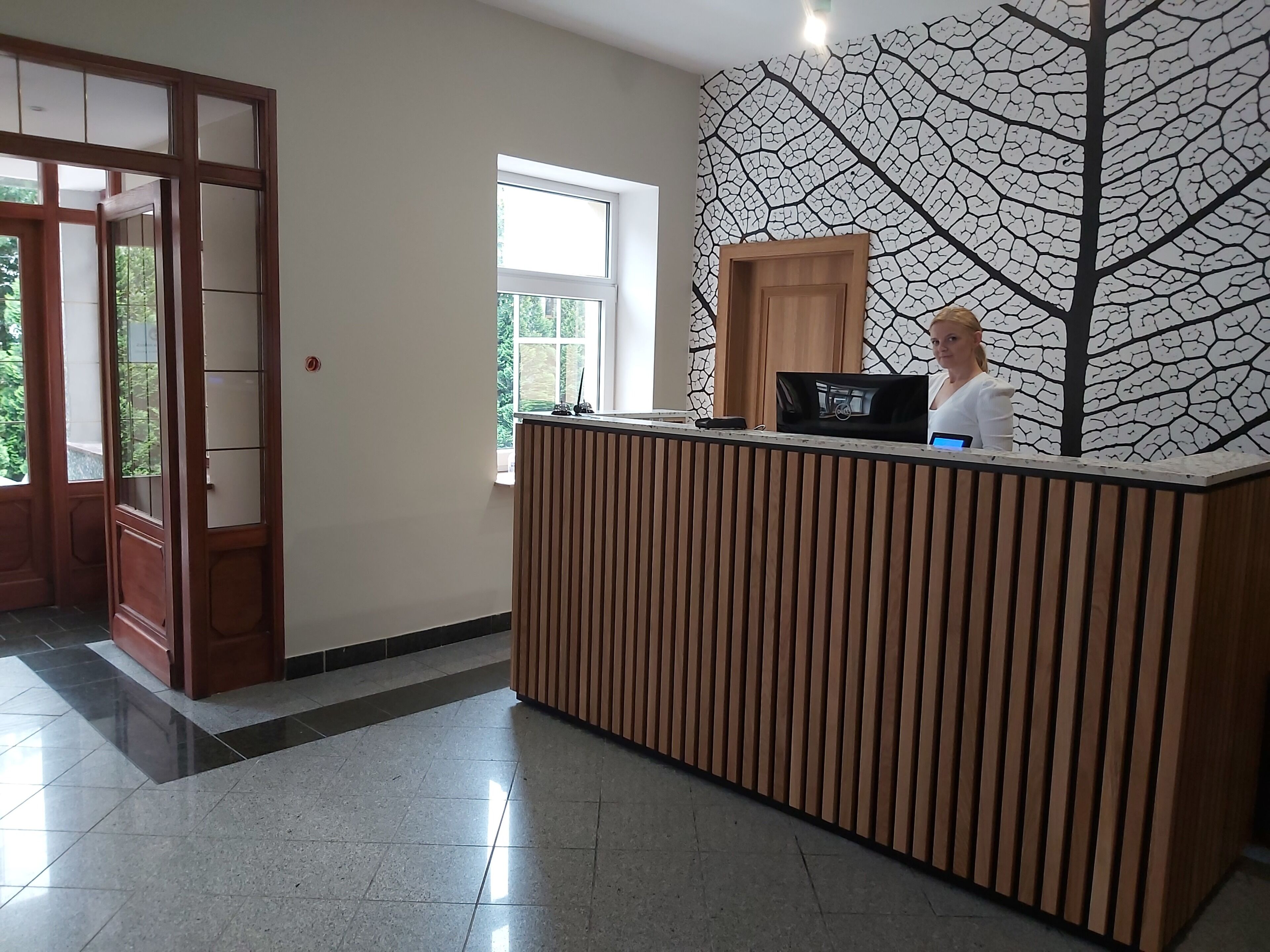 Ein Empfangsschalter mit Holzvertäfelung, ein großes Fenster und eine Wand mit Blattmuster.