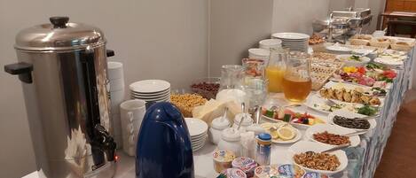 A buffet table with various food items, a coffee maker, and condiments.