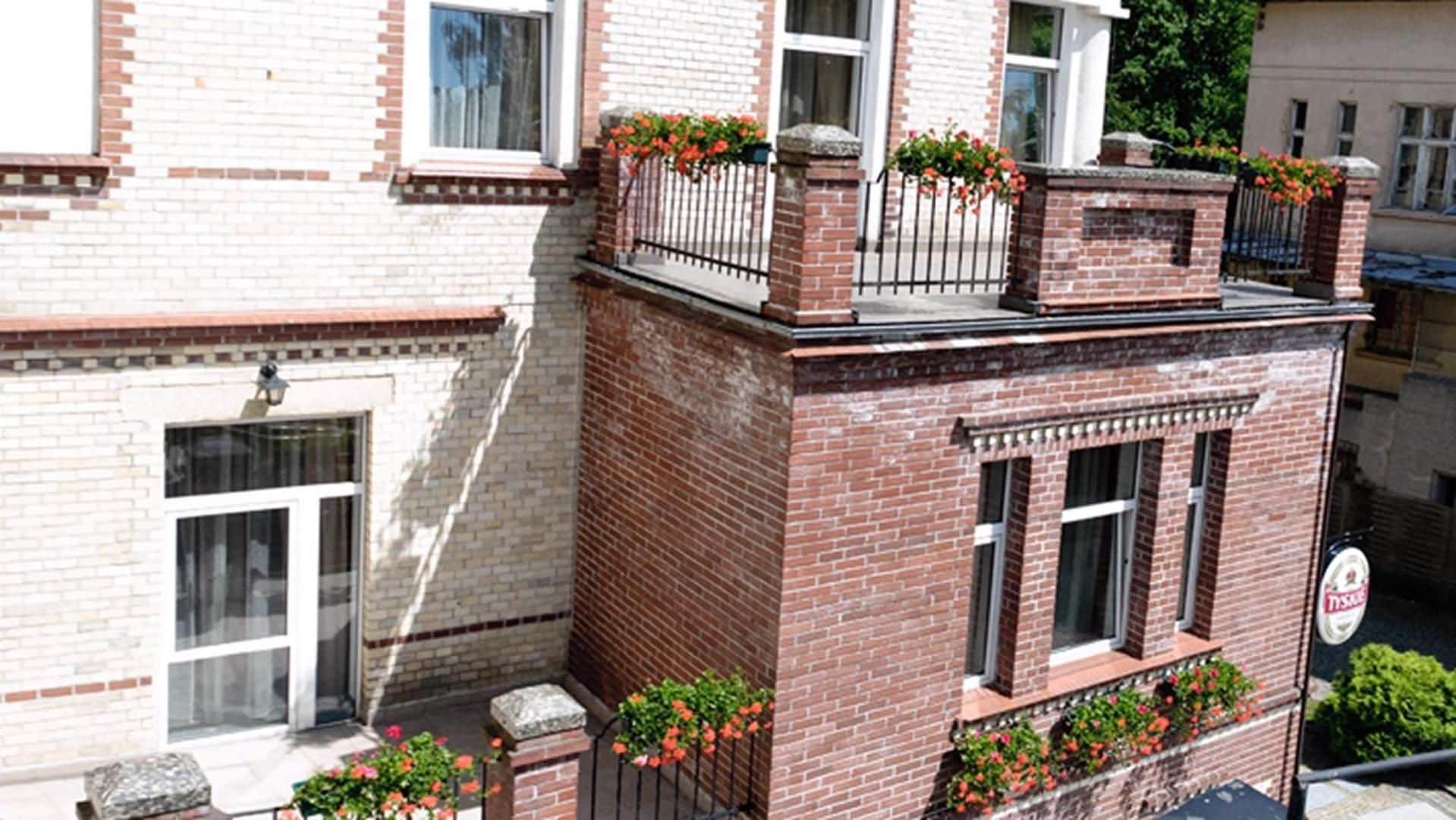A two-story building with a brick facade, a small balcony with flower boxes, and a visible window with a sign.