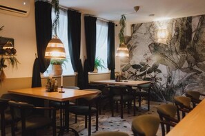 A dining area with tables and chairs, a wall mural, hanging lamps, and potted plants. - Park Hotel (Swidnica)