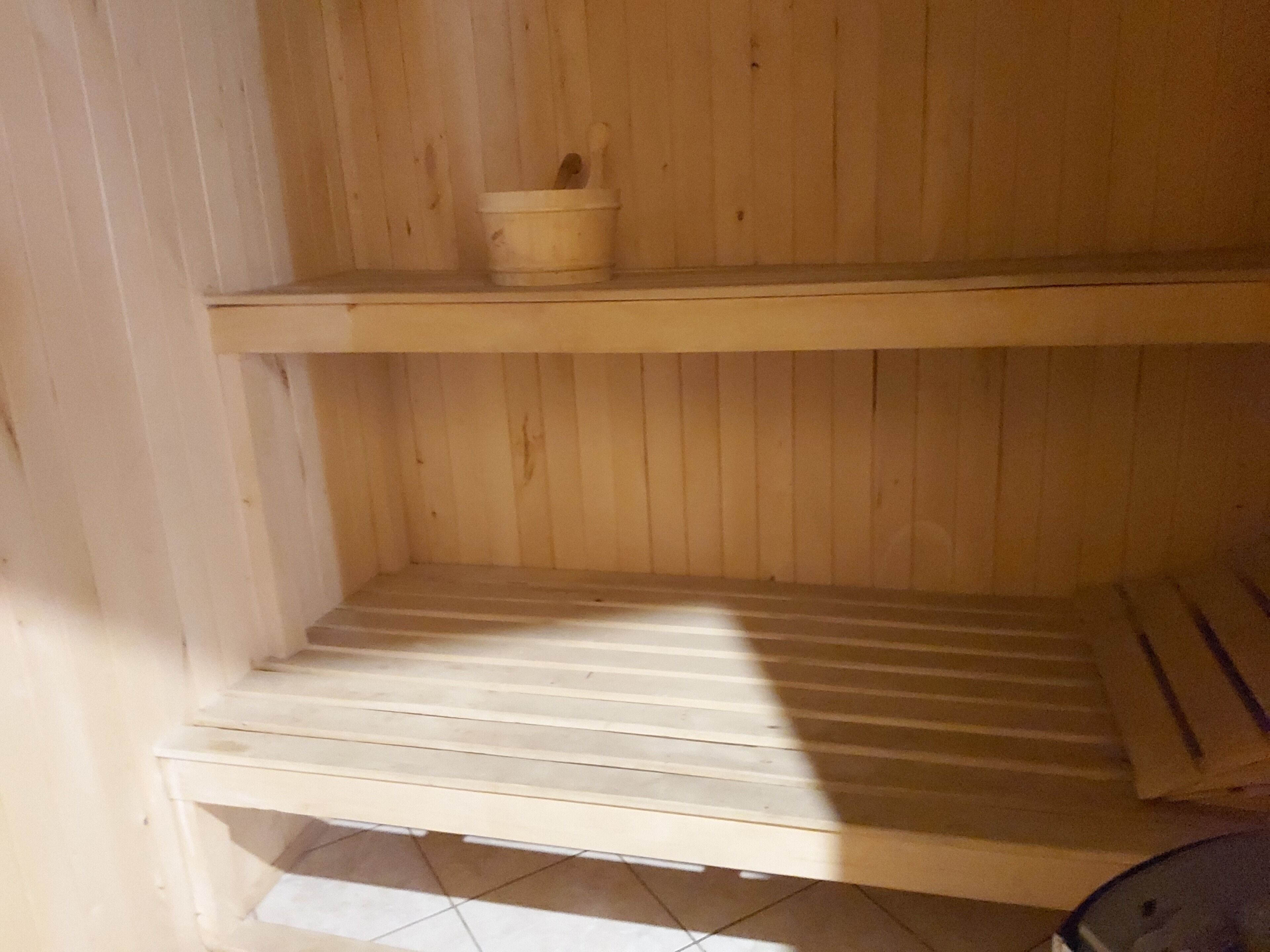 A wooden sauna with a bench and a small bucket.
