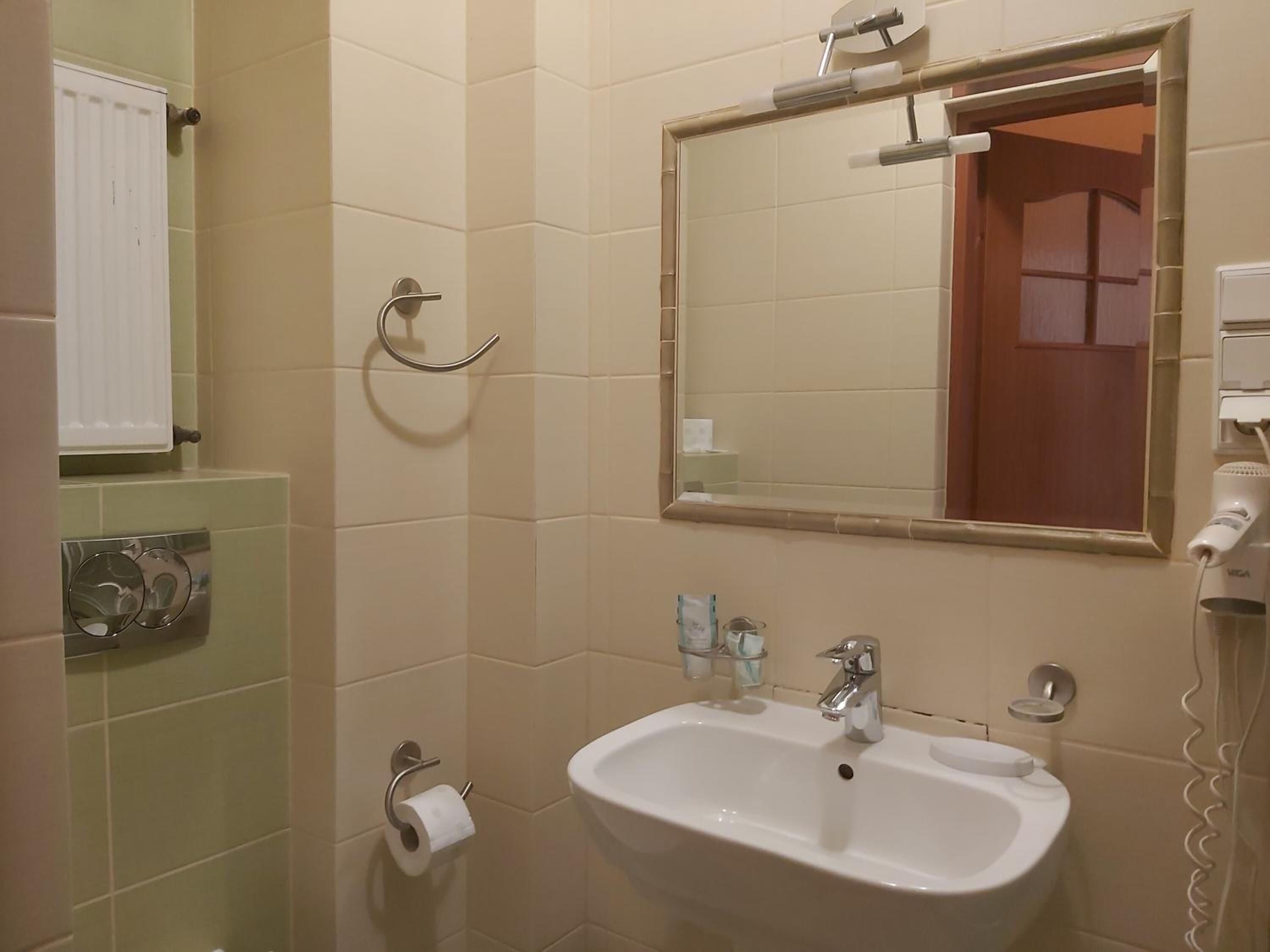 A bathroom with a sink, mirror, towel rack, and toilet paper.
