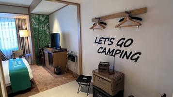 Hotelkamer met een bed, bureau, televisie en een muur met de tekst 'LET'S GO CAMPING'.