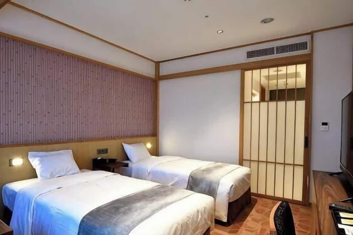 A hotel room with two beds, a wooden headboard, a sliding door, and a television.