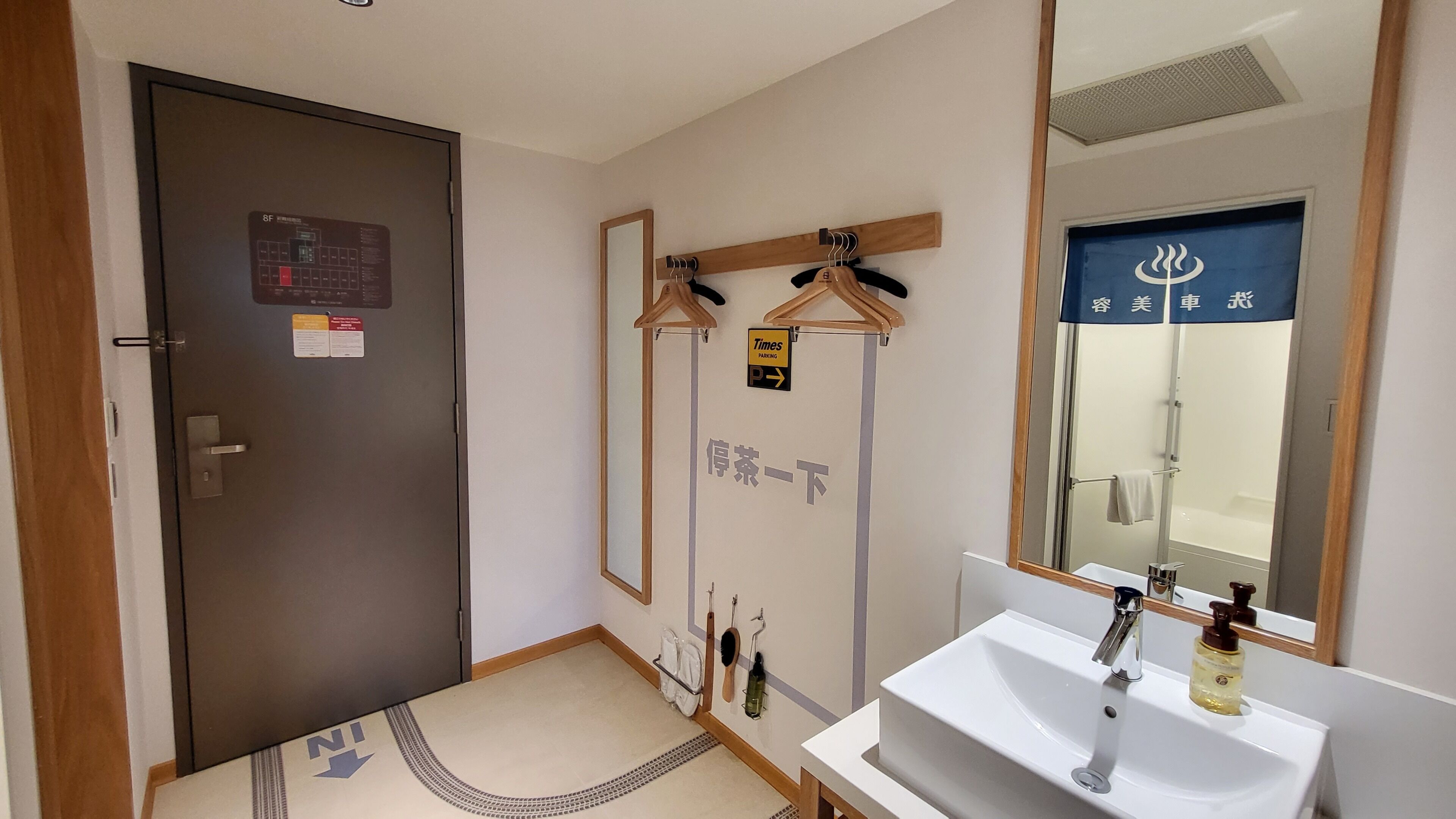 A bathroom with a sink, mirror, towel rack, and a door with a Times Parking sign.