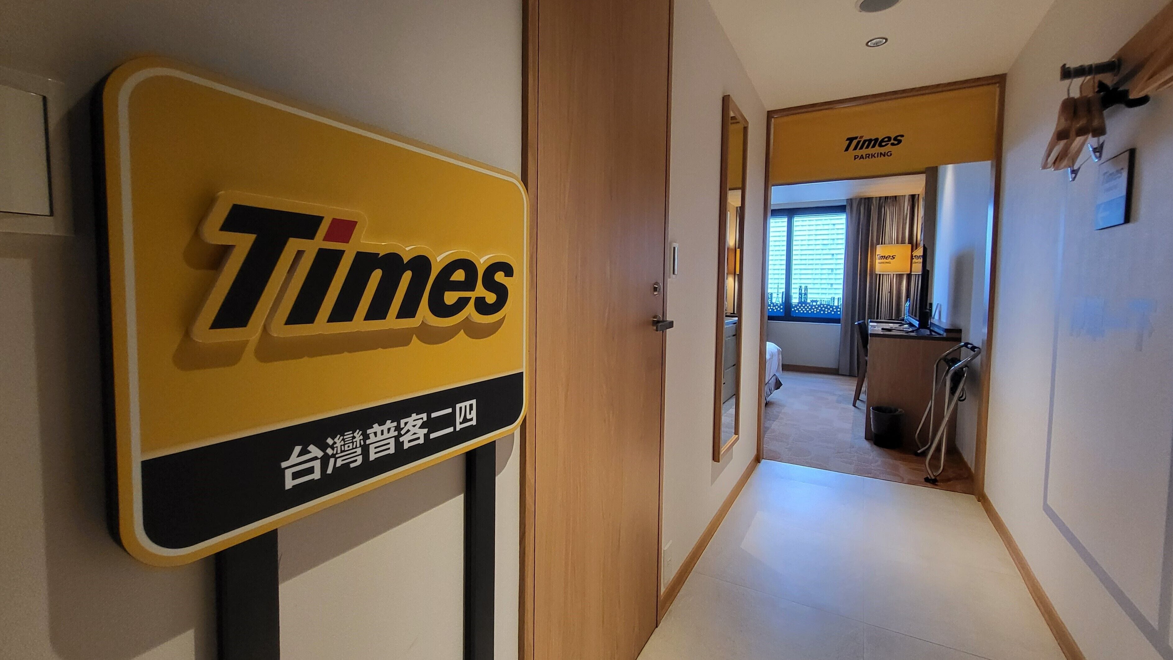 A hotel corridor with a Times Parking sign, a bed, a desk, and a window with curtains.