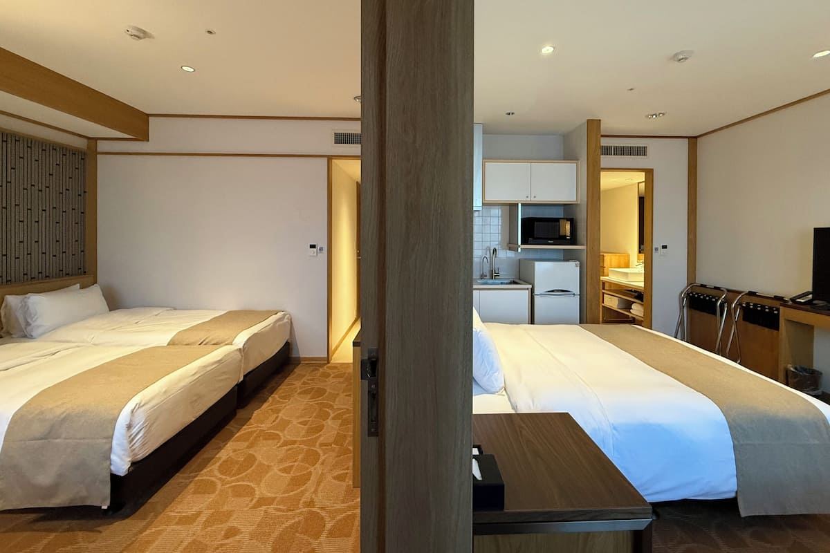 A hotel room with two beds, a small kitchenette, and a TV.
