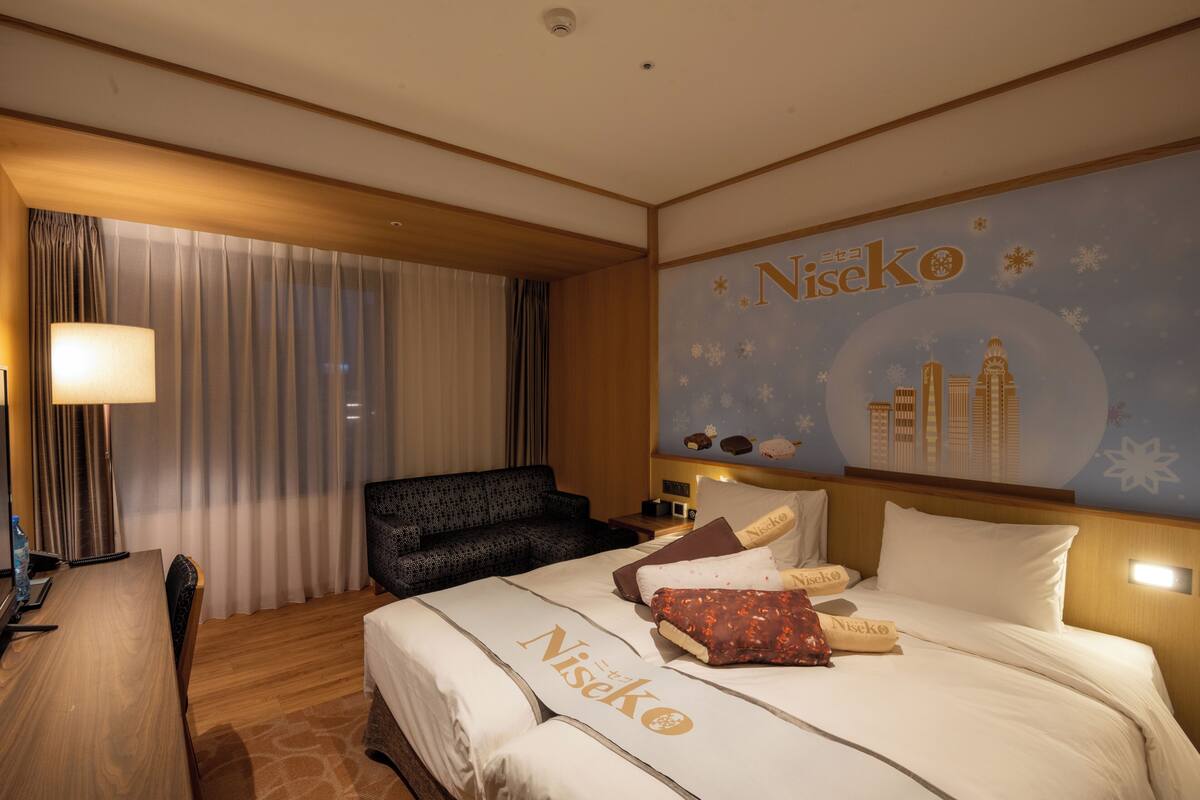 A hotel room with a bed, a desk, a chair, a sofa, and a wall with the hotel's name.