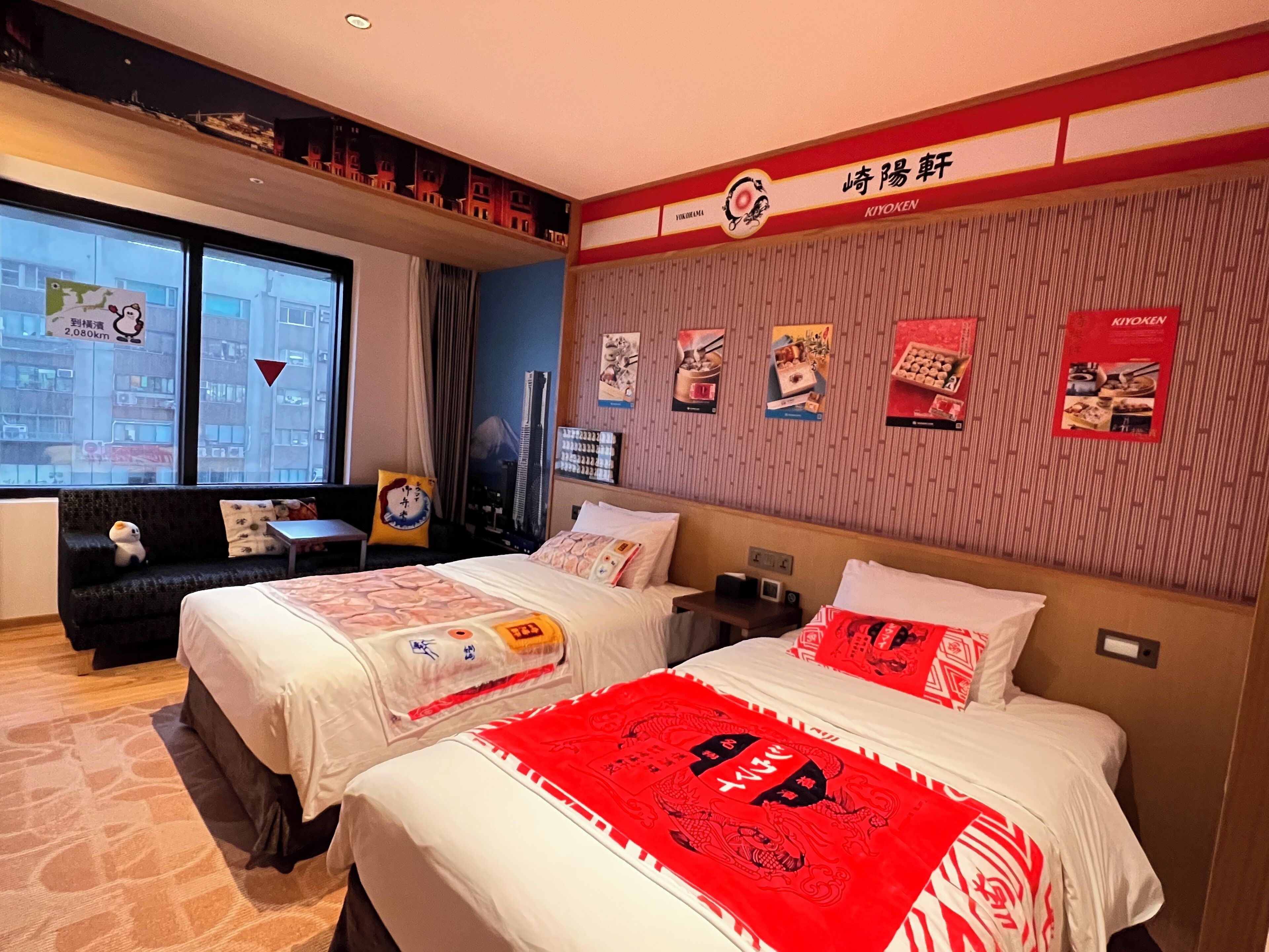 A hotel room with two beds, a sofa, a TV, and a window with a view of buildings.