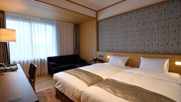 A hotel room with a large bed, a desk, and a chair. There is a window with curtains, a wall with vertical lines, and a lamp on the desk.