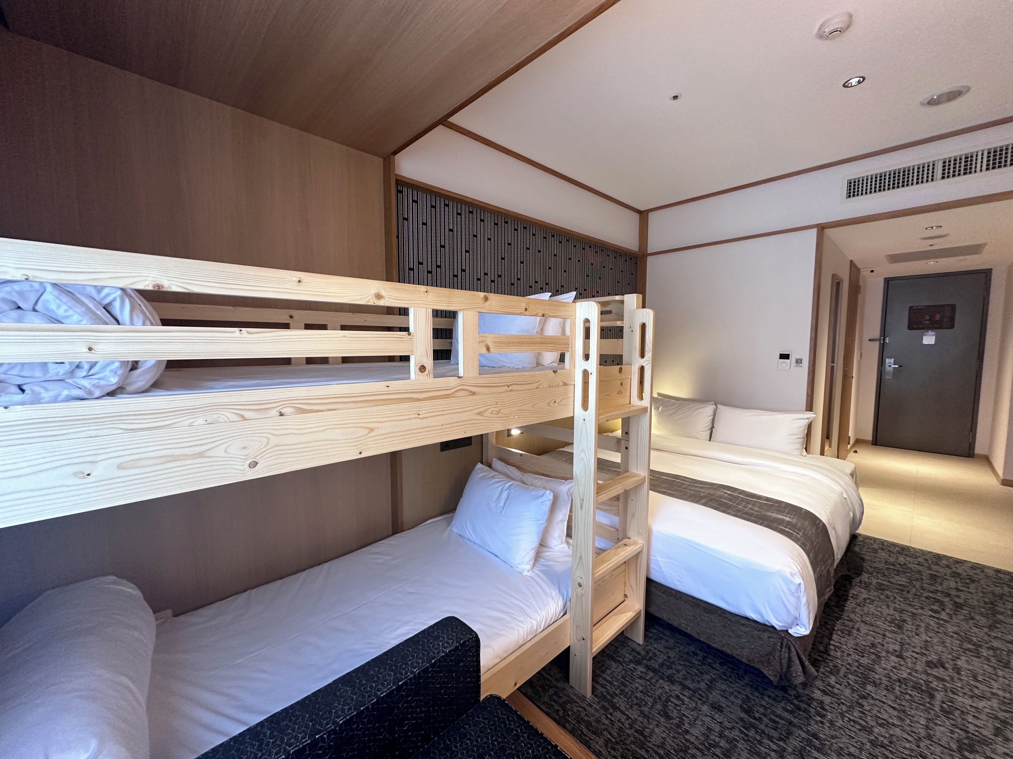 A hotel room with bunk beds, a sofa, and a door.