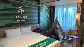 A hotel room with a bed, a green wall with the 'HANDS' logo, a teepee, and a view of trees through the window.