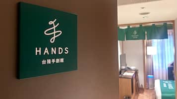A hotel room with a green sign on the wall, a bed with a green cover, a desk, and a chair.