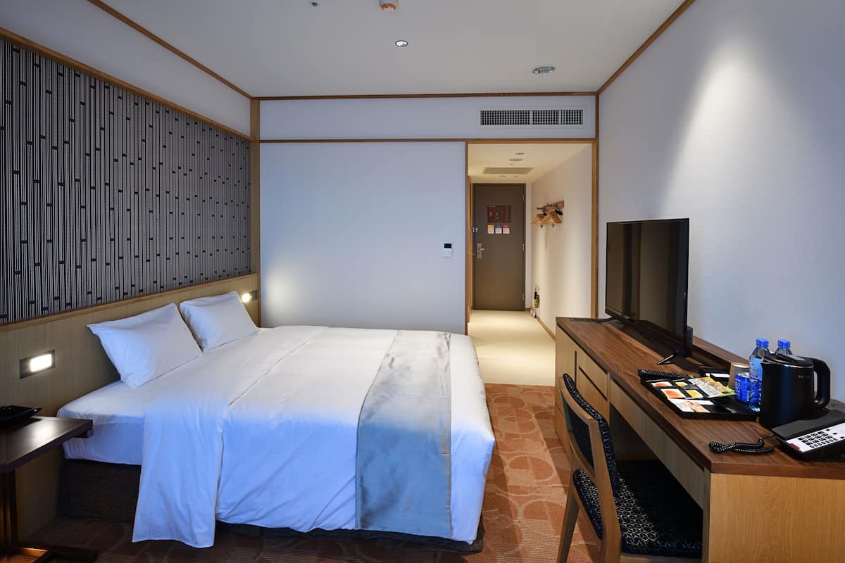 A hotel room with a bed, a desk with a computer, a TV, and a coffee maker.