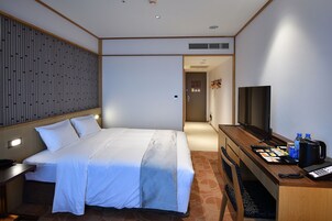 A hotel room with a bed, a desk with a computer, a TV, and a coffee maker.