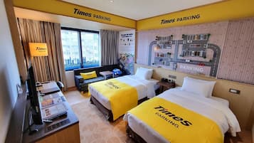 A hotel room with two beds, a desk, a TV, a window with curtains, and a Times Parking sign on the wall.