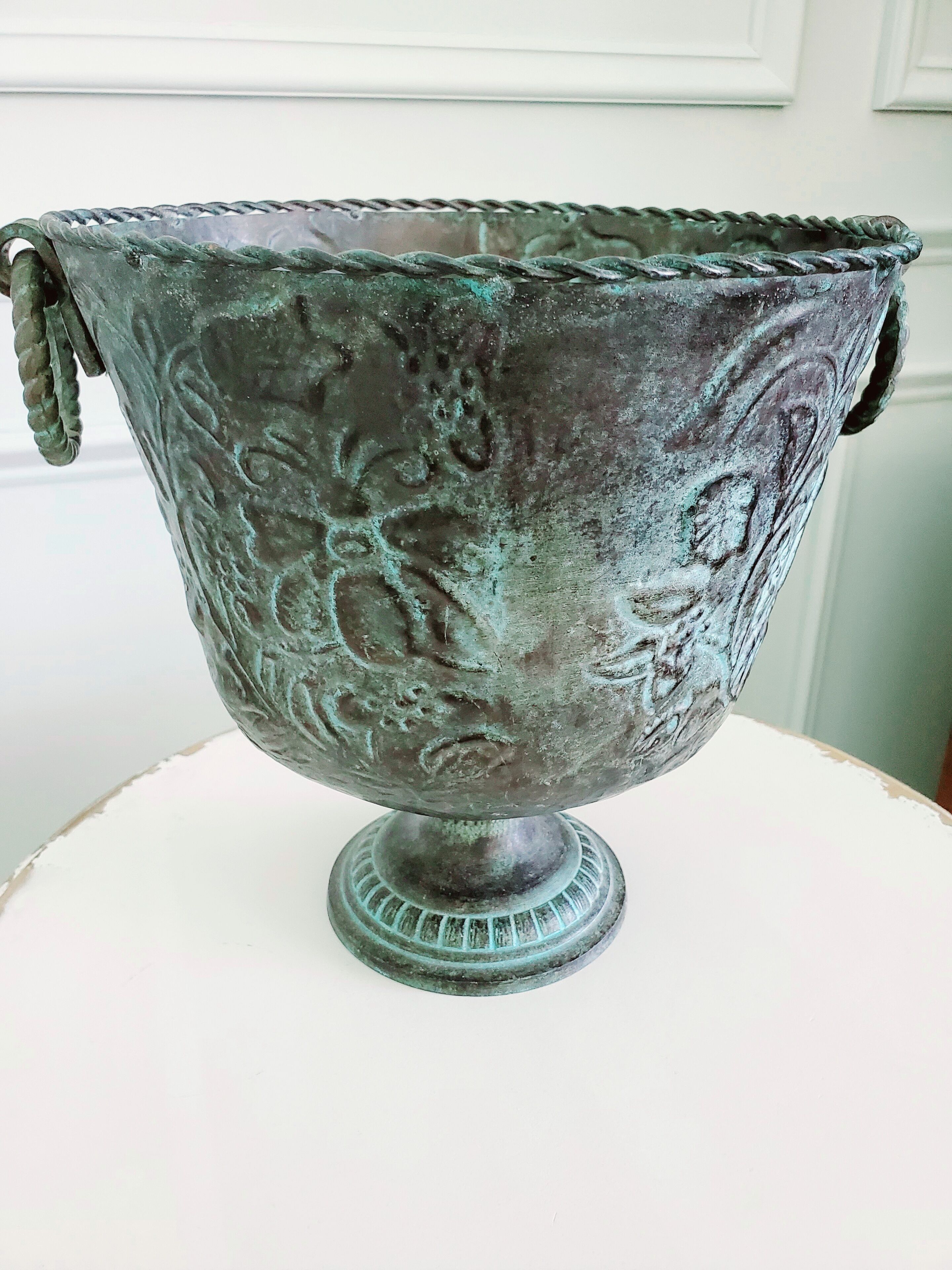 A metal bowl with intricate designs, placed on a white pedestal.