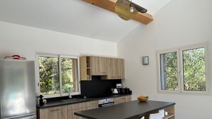 Una cocina moderna con refrigerador, gabinetes de madera, encimera negra, un fregadero, un hervidor y un bol en la encimera.