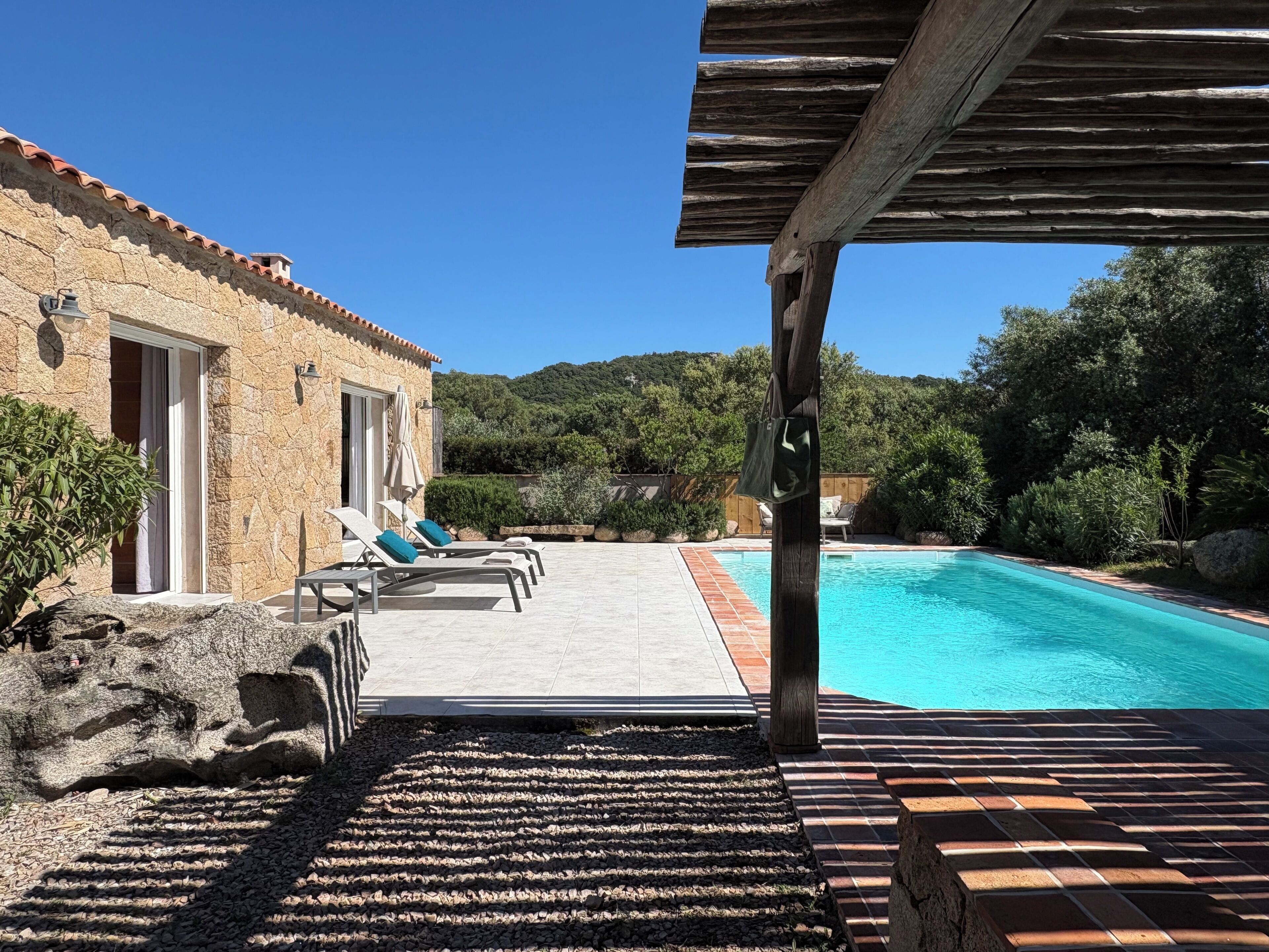 A stone building with a pool, outdoor seating, and a view of the surrounding hills.