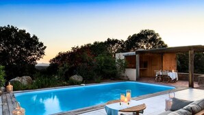 Piscina con terraza de madera, asientos exteriores y un área cubierta con mesas y sillas.