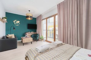 Et moderne soveværelse med seng, skrivebord, sofa, fjernsyn og et stort vindue.