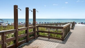 A wooden boardwalk leading to a beach with umbrellas and people.