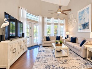 A living room with a flat-screen TV, two sofas, a coffee table, and a ceiling fan.