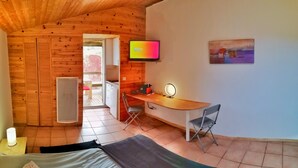 Una habitación acogedora con paredes de madera, una cama, un escritorio con una silla, un televisor y un cuadro en la pared.