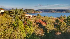 Un paisaje costero con un edificio rodeado de vegetación densa y colinas al fondo.