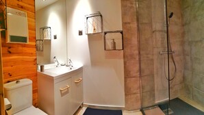 Un baño moderno con un tocador blanco, un espejo grande, cabina de ducha con paredes de vidrio y paneles de madera en las paredes.